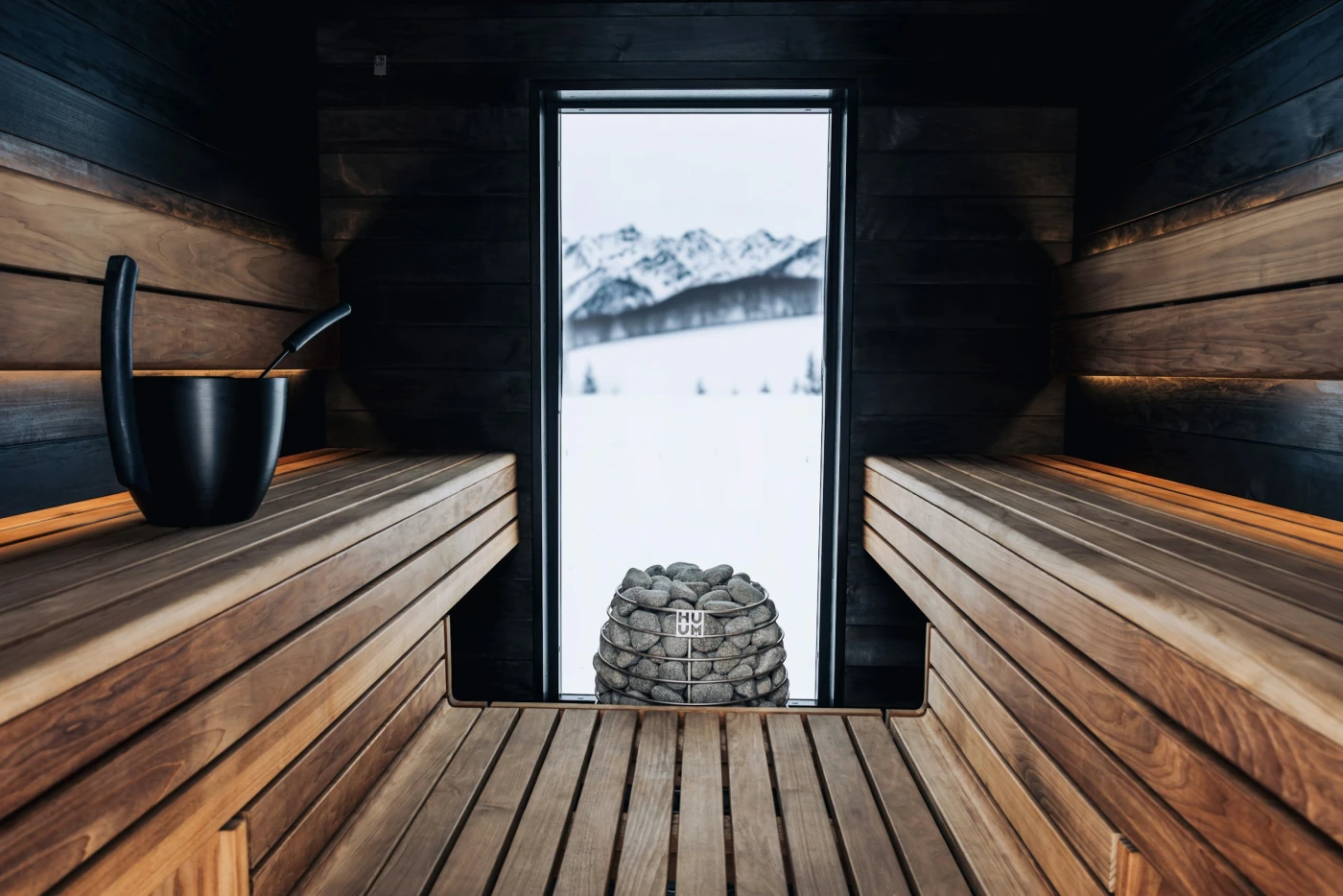De sauna van binnen: twee houten banken en een raam op het landschap.